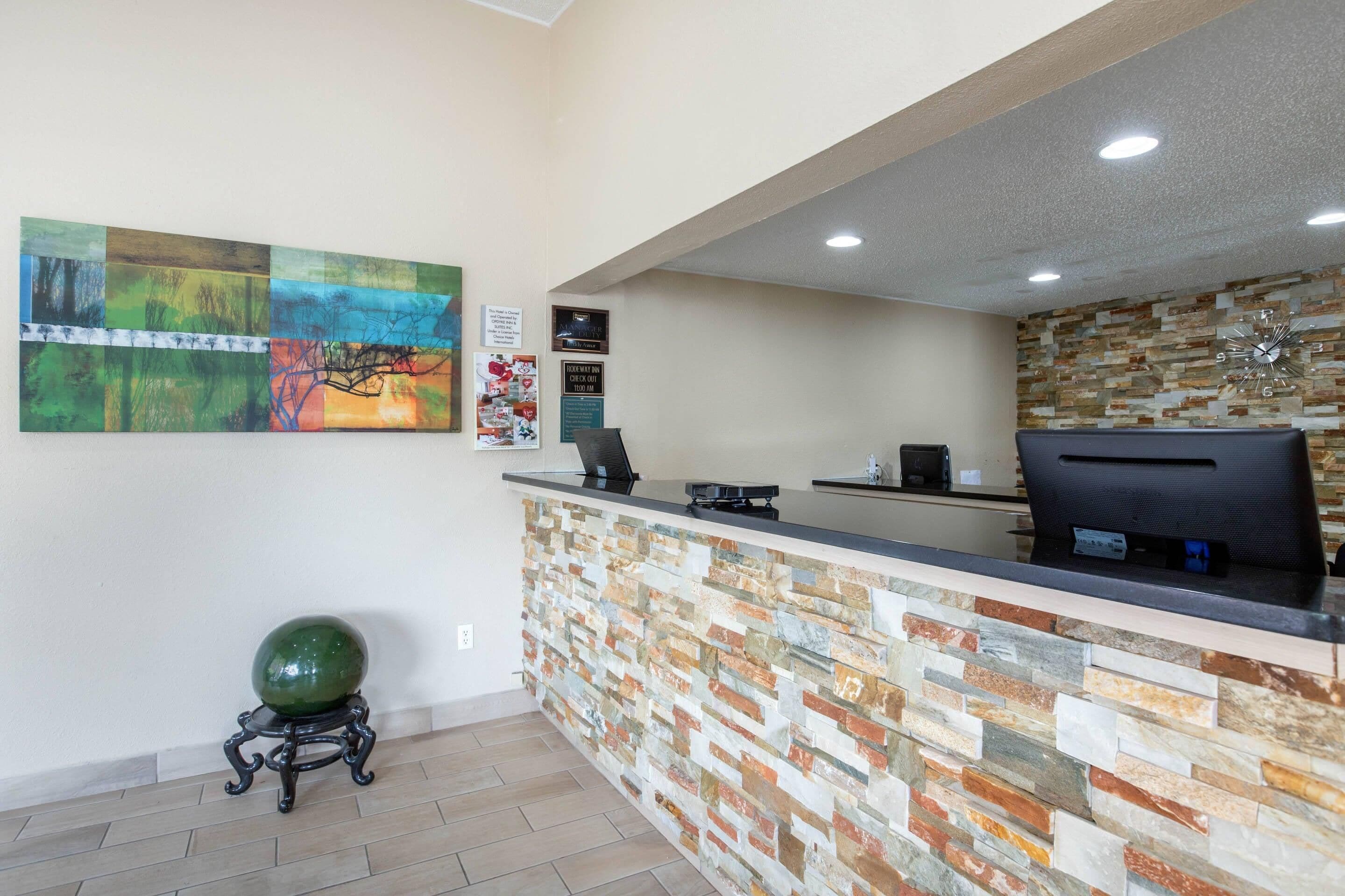 A reception desk with a stone wall, a clock, and a green spherical object on a stand.
