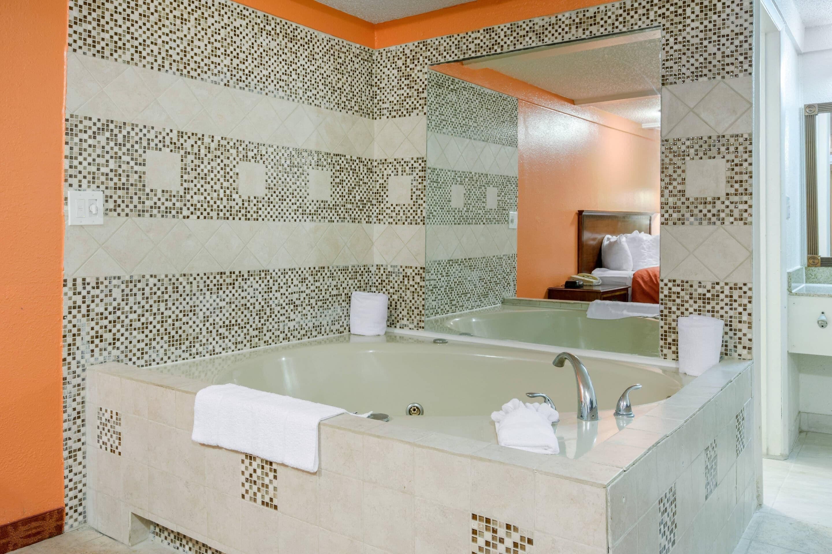 A bathroom with a large bathtub, a mirror, and a sink.