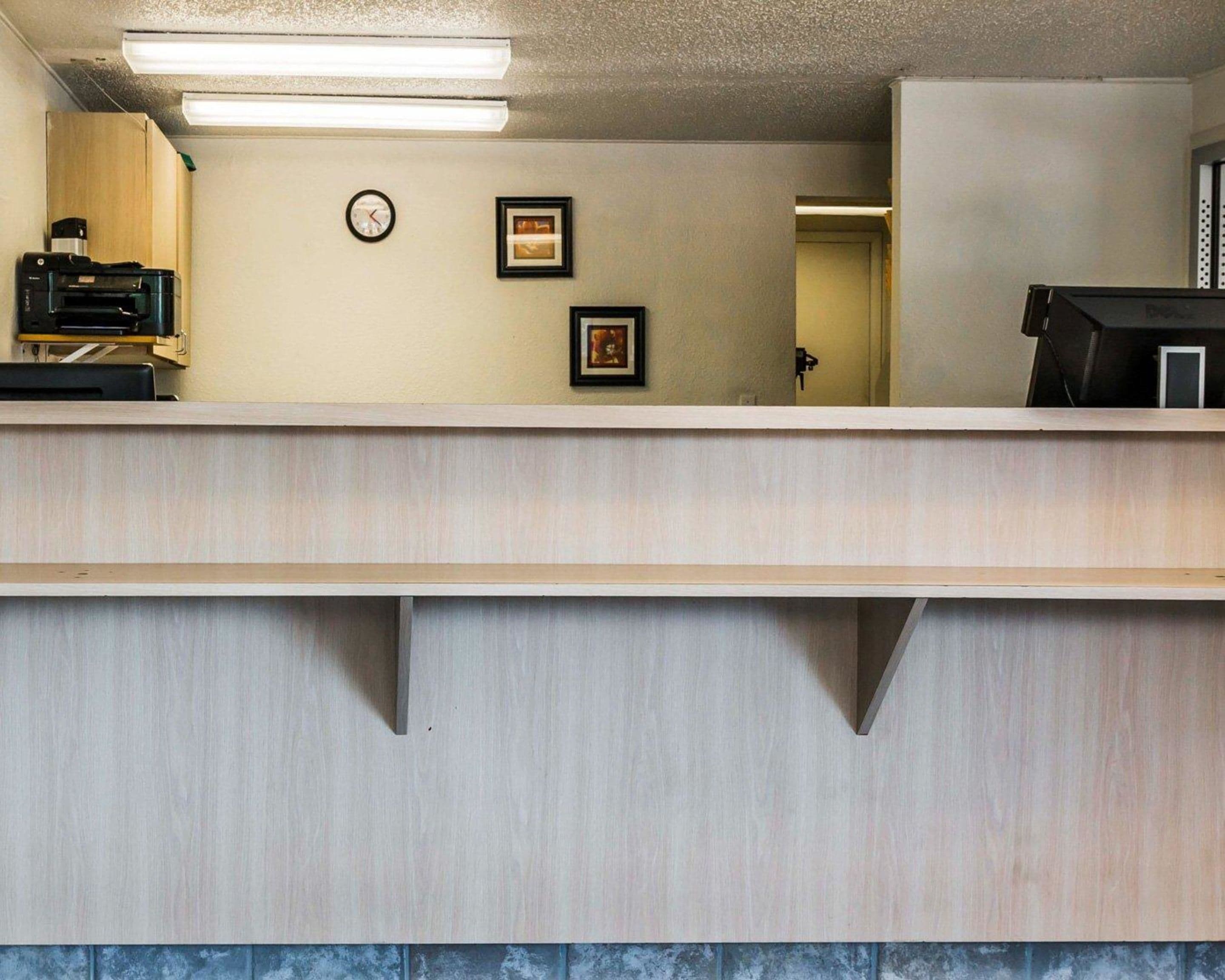 Un espace d’accueil avec un comptoir de réception, une horloge, des tableaux encadrés et une imprimante.