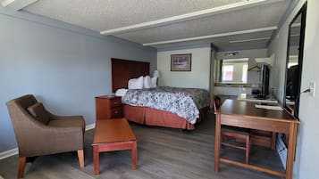 Una habitación con cama, una silla, una mesa y un escritorio con computadora.