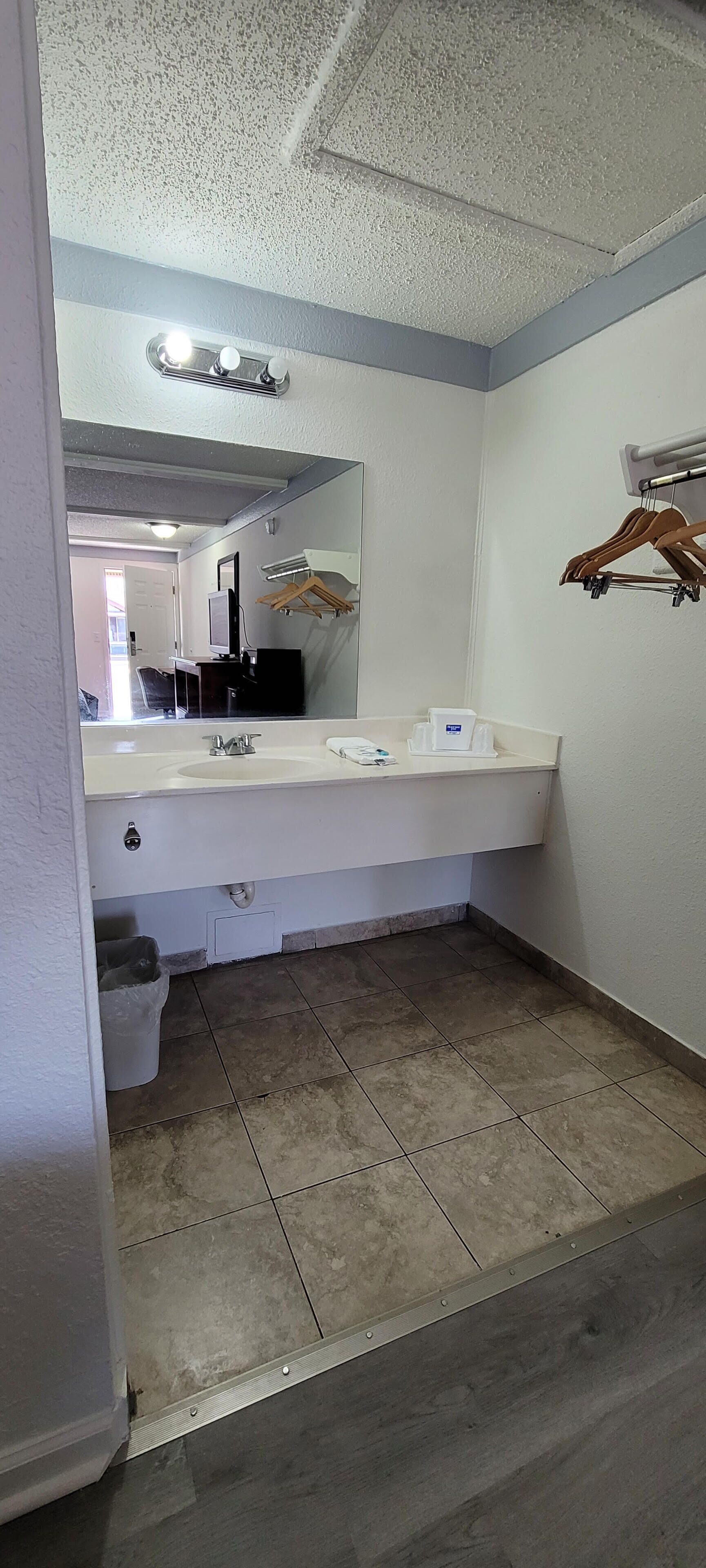 A bathroom with a white sink, mirror, and a wooden hanger rack.