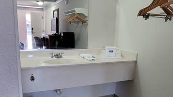 A bathroom with a white sink, mirror, and a wooden hanger rack.