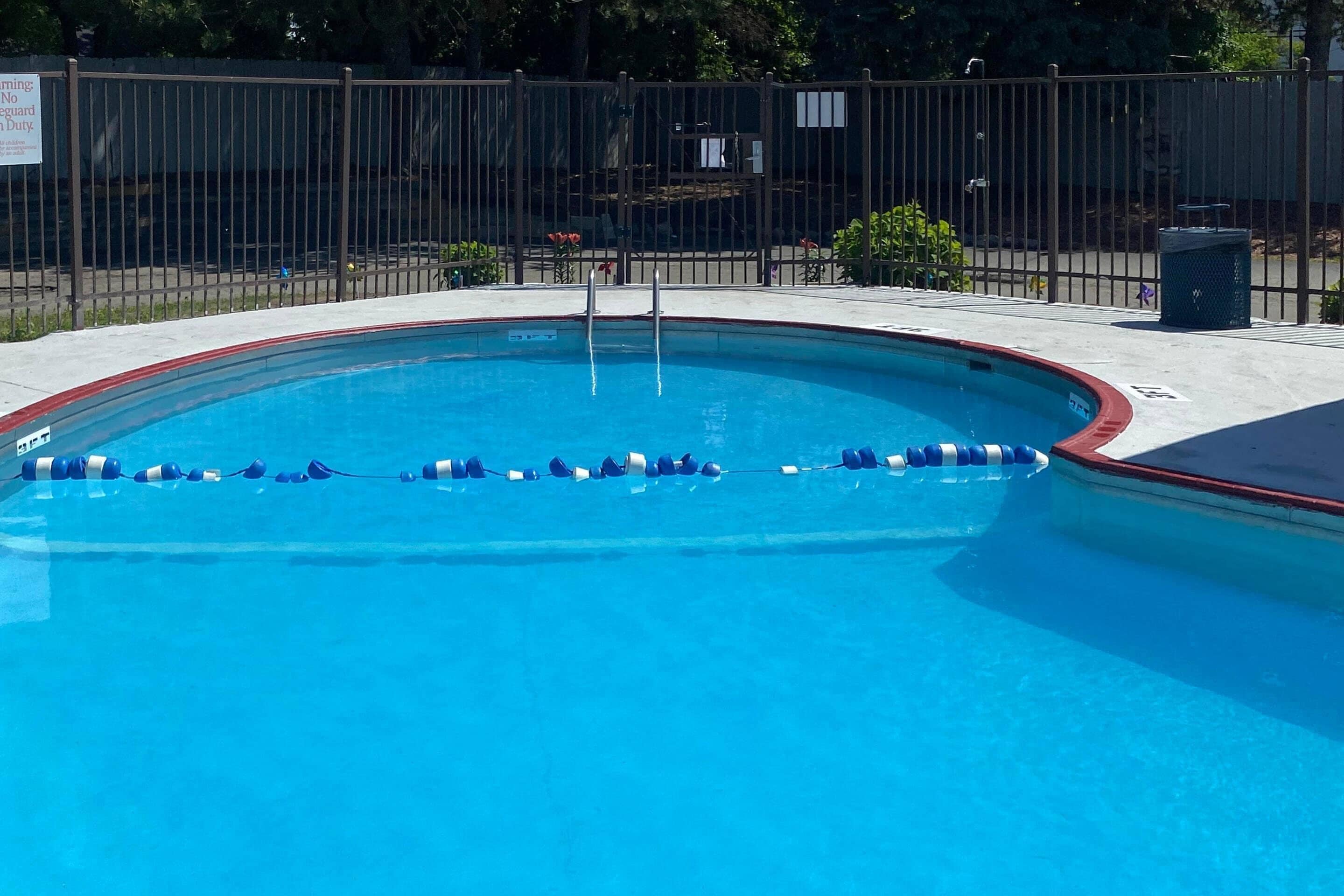 A swimming pool with a metal fence, a lifeguard sign, and a trash can.