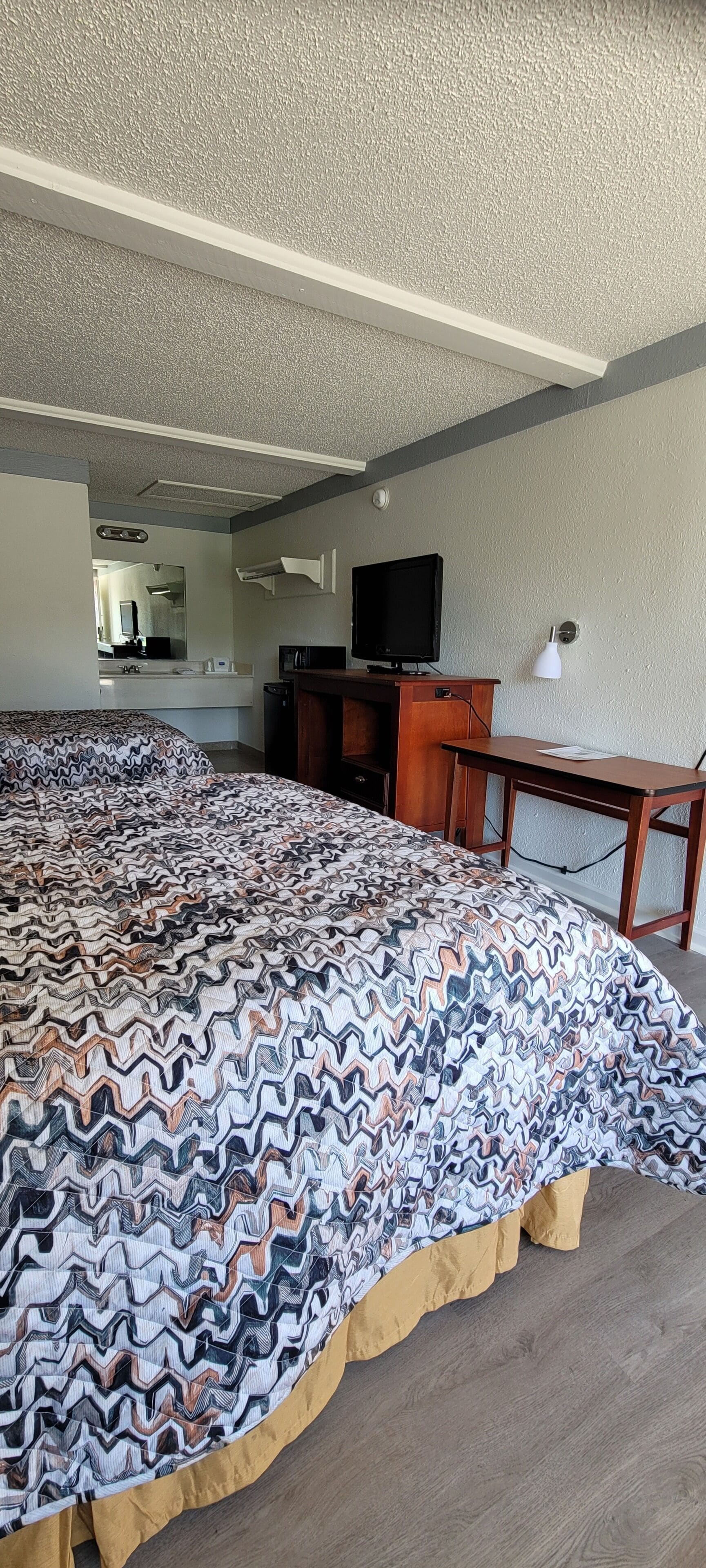 Een hotelkamer met een groot bed, een bureau, een televisie en een spiegel.