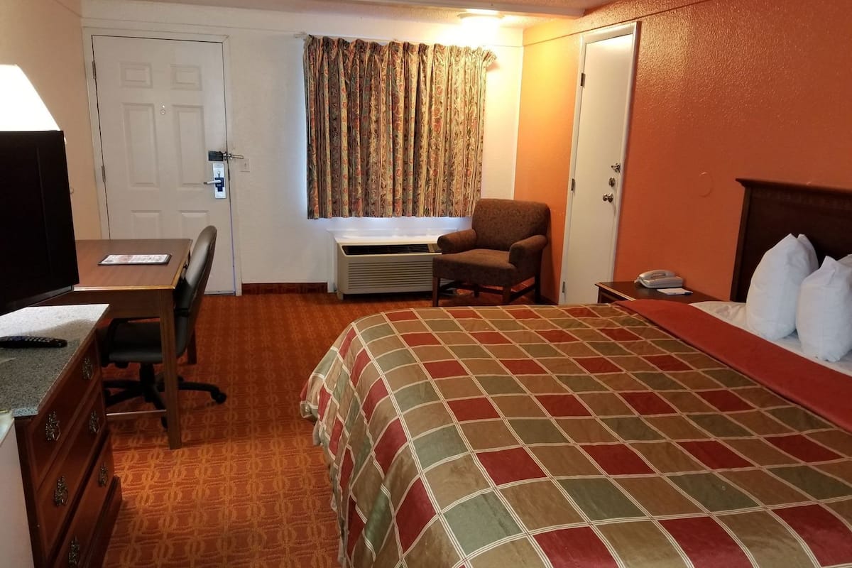 A hotel room with a bed, a desk, a chair, a TV, and a window with curtains.