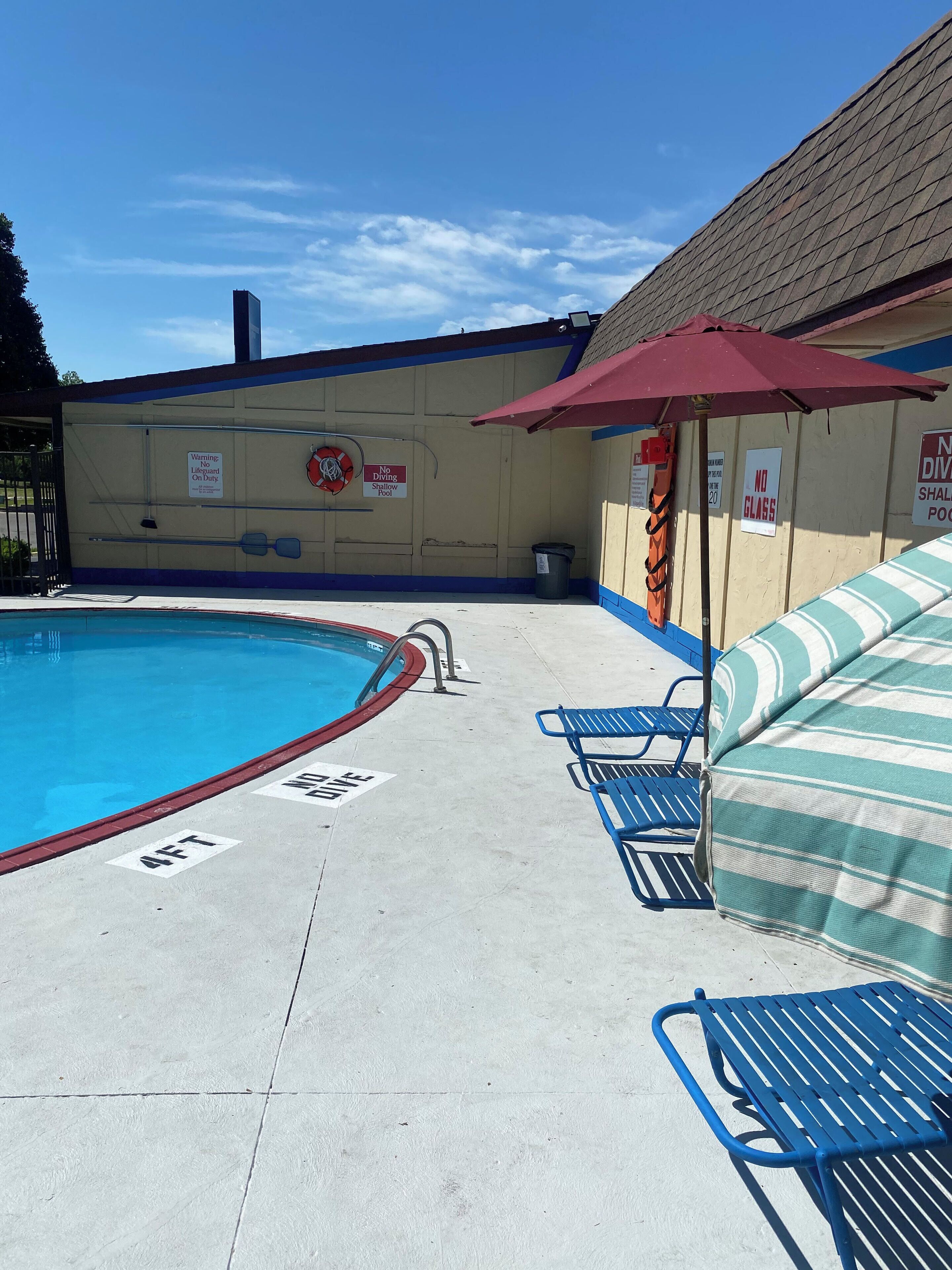 A swimming pool with a lifeguard stand, lounge chairs, and a no diving sign.