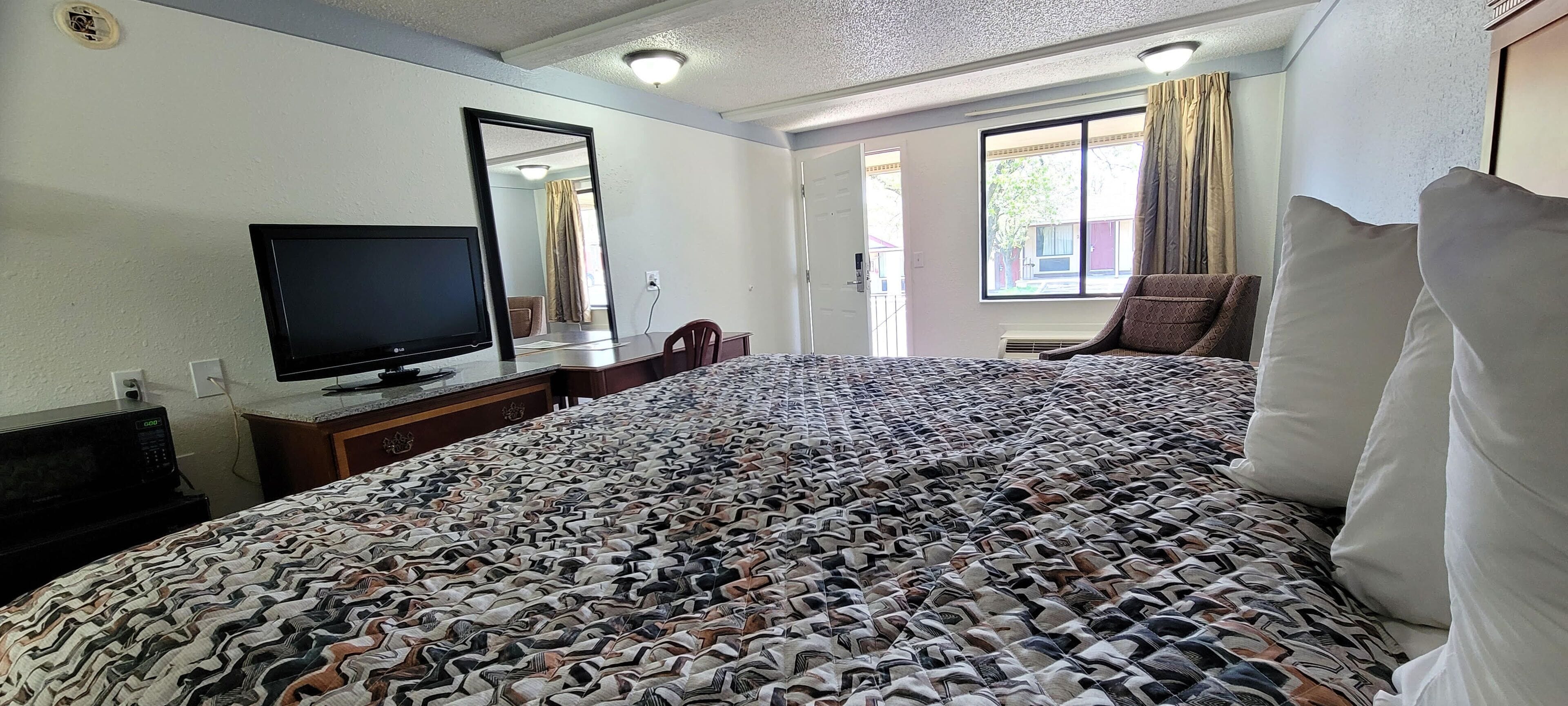 Habitación de hotel con una cama grande, un escritorio, un televisor de pantalla plana, una silla y una ventana con cortinas.
