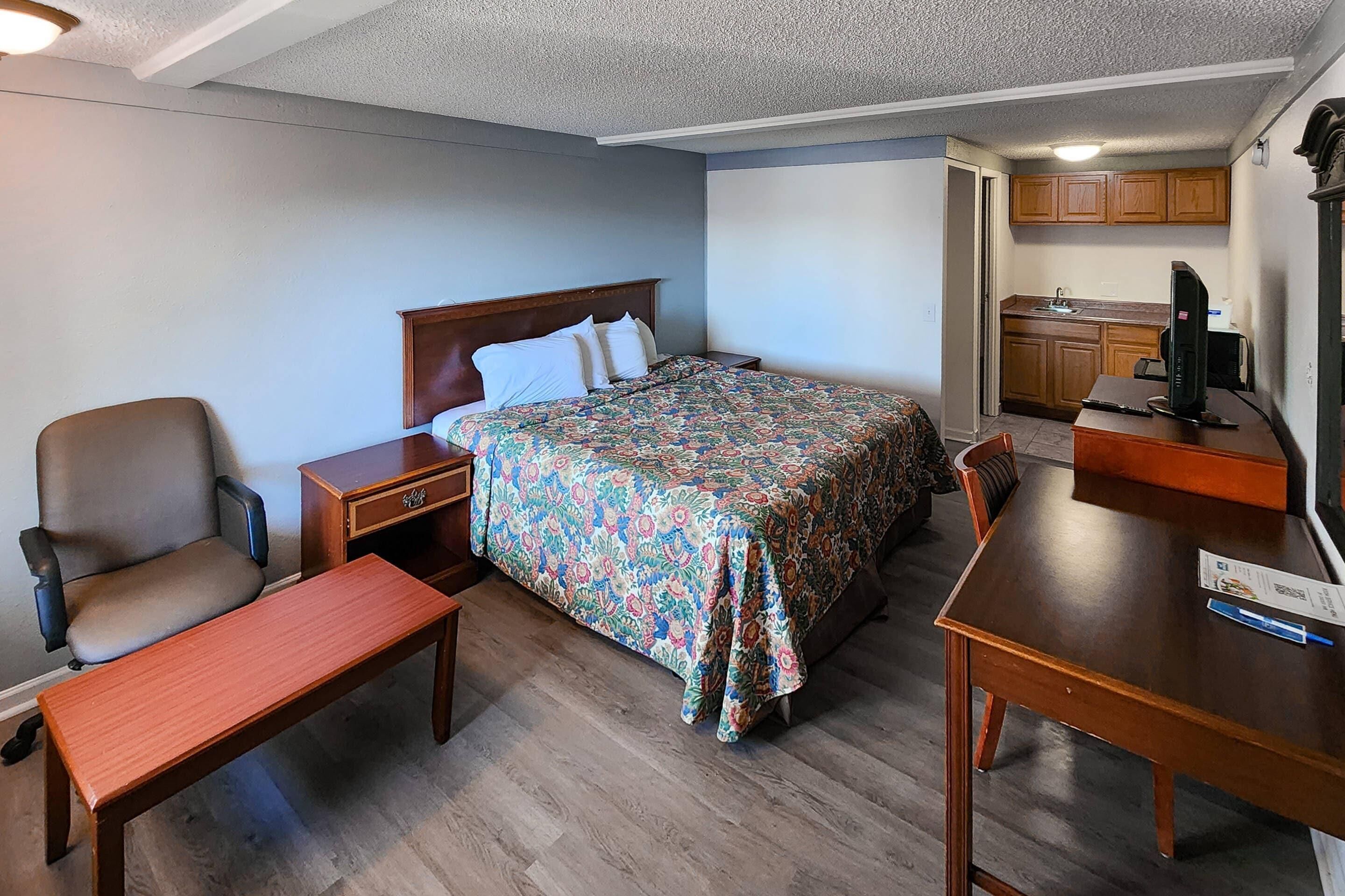 Une chambre comprenant un lit, un bureau, une chaise, une table de chevet et une petite kitchenette.