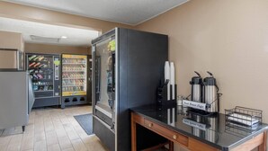 Una kitchenette con refrigerador, máquina de café y expendedor.