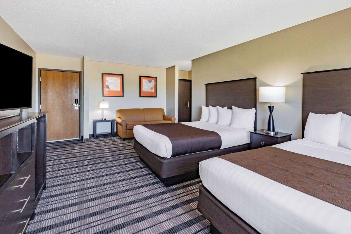 A hotel room with two beds, a sofa, a TV, and framed pictures on the wall.