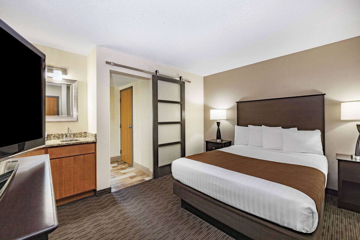 A hotel room with a bed, a desk, a TV, a wardrobe, and a bathroom door.