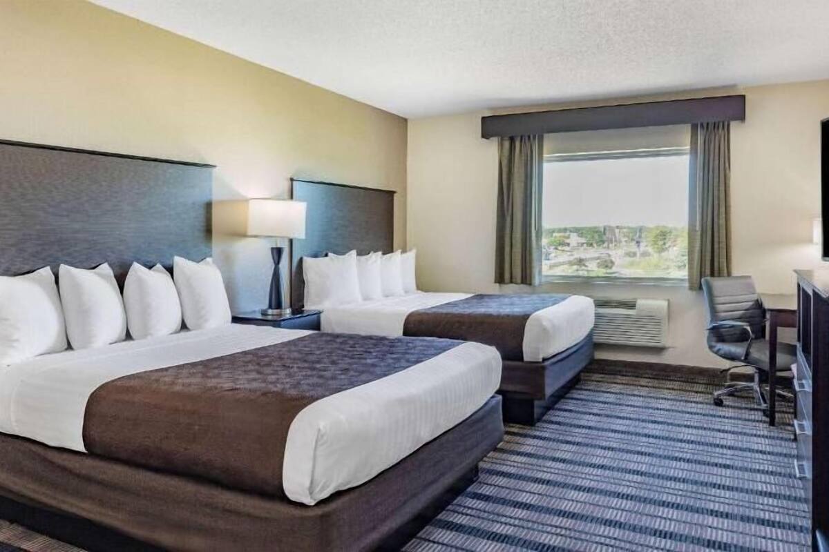 A hotel room with two beds, a desk, a TV, and a window with a view.
