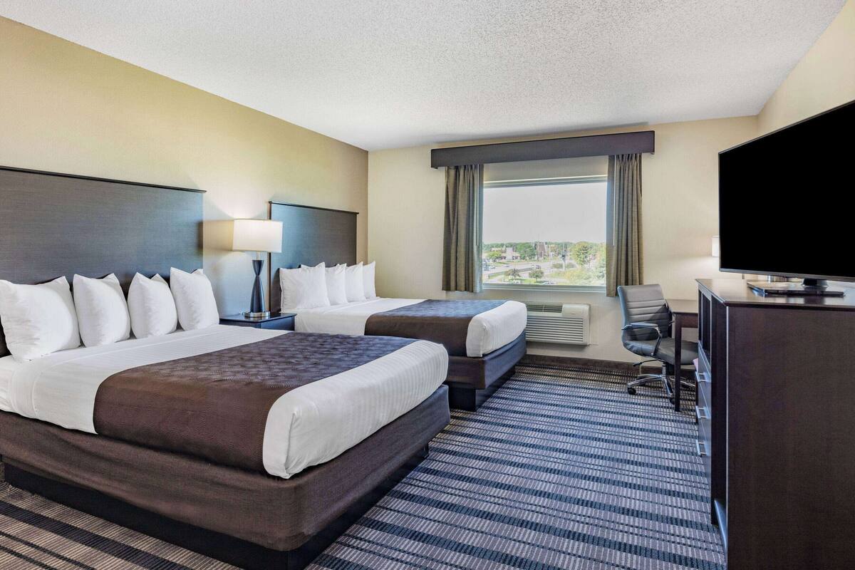A hotel room with two beds, a desk, a television, and a large window with a view.