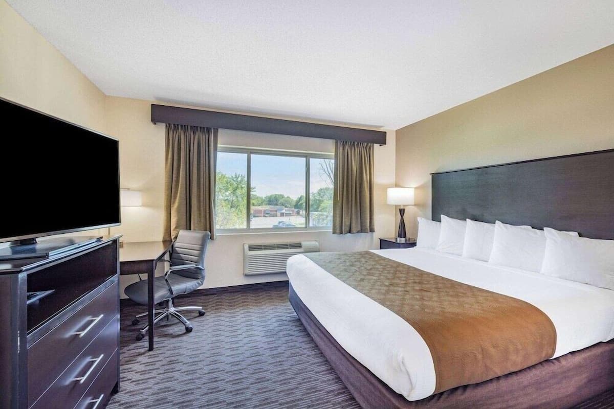 A hotel room with a large bed, a desk, a television, and a window with curtains.