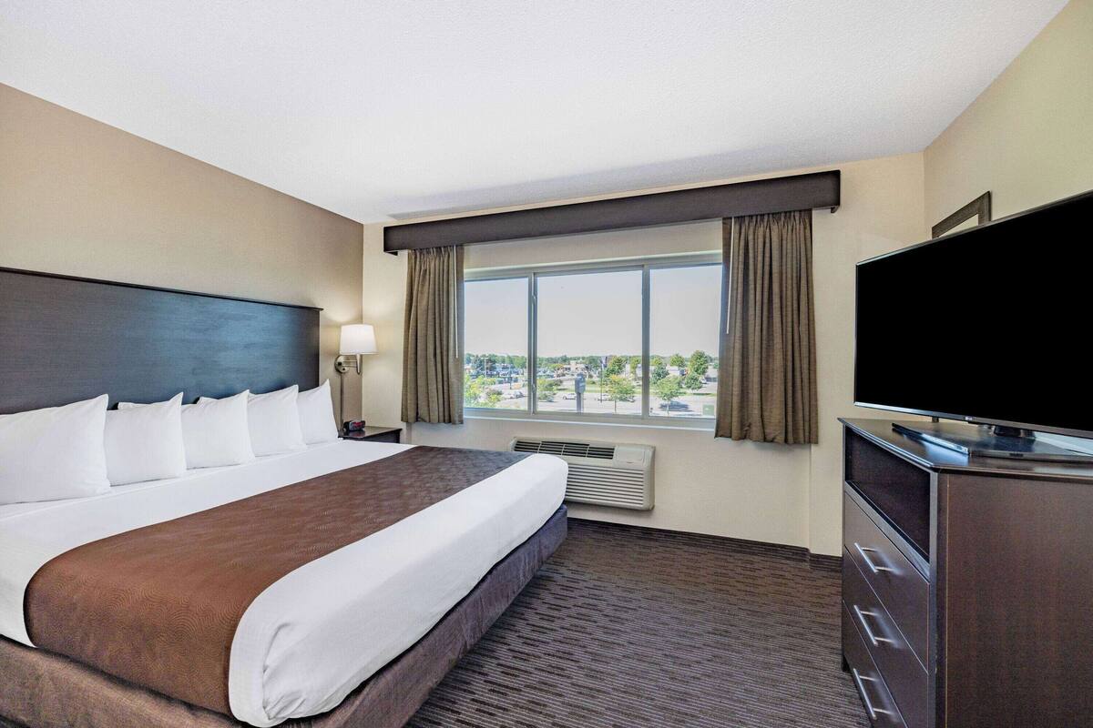 A hotel room with a large bed, a flat-screen TV, a dresser, and a window with curtains.