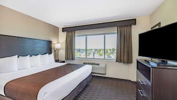 A hotel room with a large bed, a flat-screen TV, a dresser, and a window with curtains.