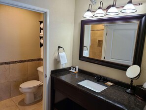 A bathroom with a toilet, sink, mirror, towel rack, and three wall-mounted lights.