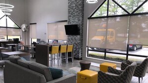 Un moderno hall de hotel con sofá, sillones, zona de bar y amplias ventanas con vistas a un aparcamiento.