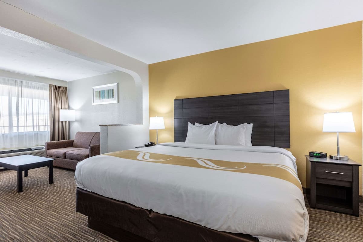Ein Hotelzimmer mit einem großen Bett, einer Couch, einem Schreibtisch und einem Nachttisch mit einer Lampe.