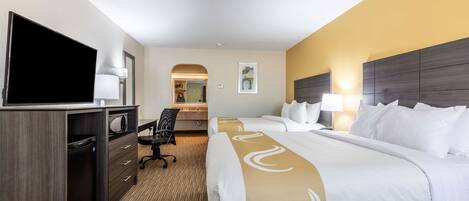 A hotel room with two beds, a desk with a flat-screen TV, a chair, a desk lamp, and a microwave.