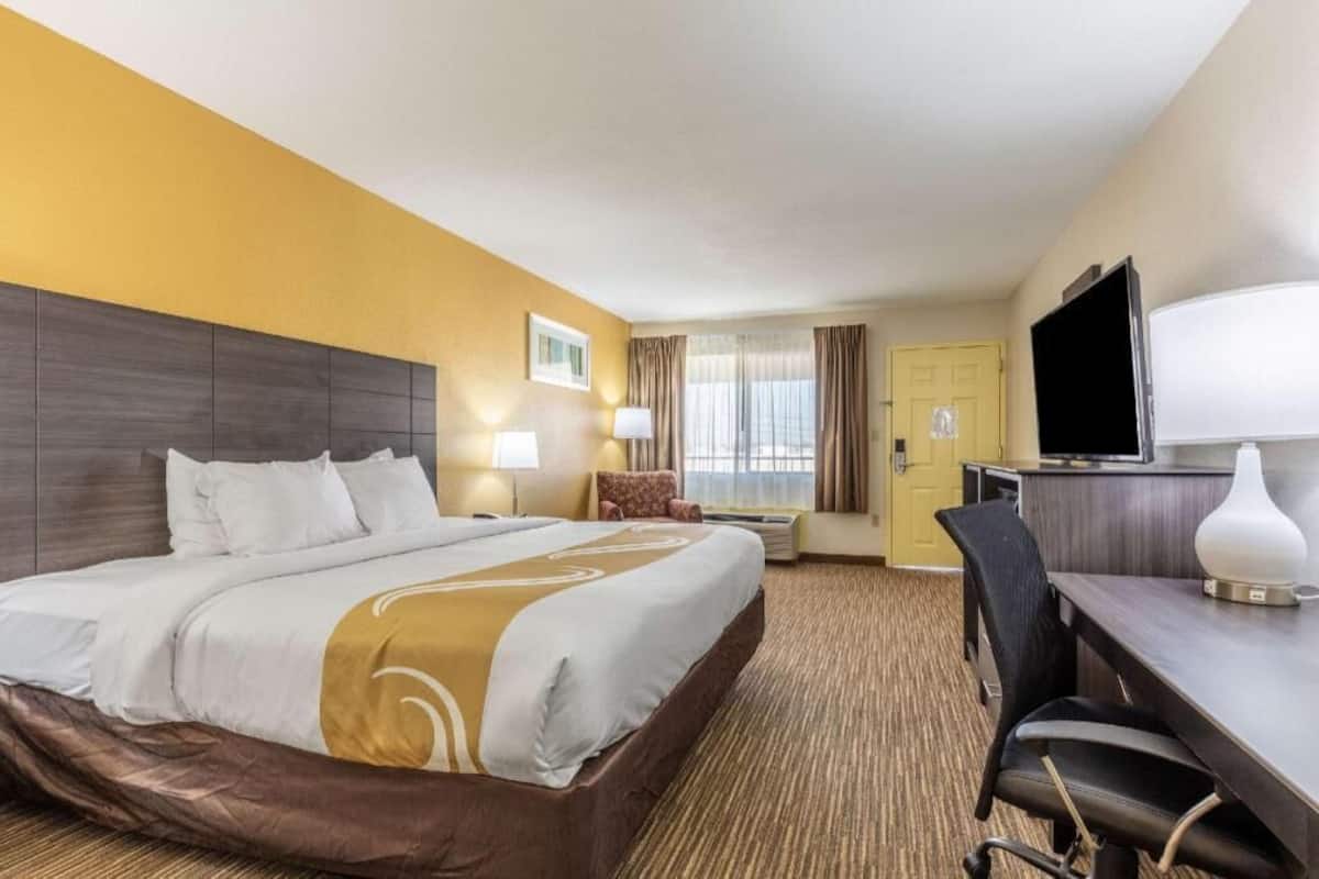 Ein Hotelzimmer mit einem großen Bett, einem Schreibtisch mit Stuhl, einem Fernseher und einer Tür.