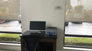 A business center with a desk, computer, printer, and a sign indicating the business center location.