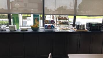 Una barra de desayuno con un bol de fruta, una máquina de café y una vitrina con pasteles.