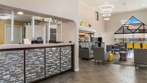 Un área de recepción moderna con un panel de vidrio, mostrador y zona de estar con sillas estampadas y una mesa amarilla.