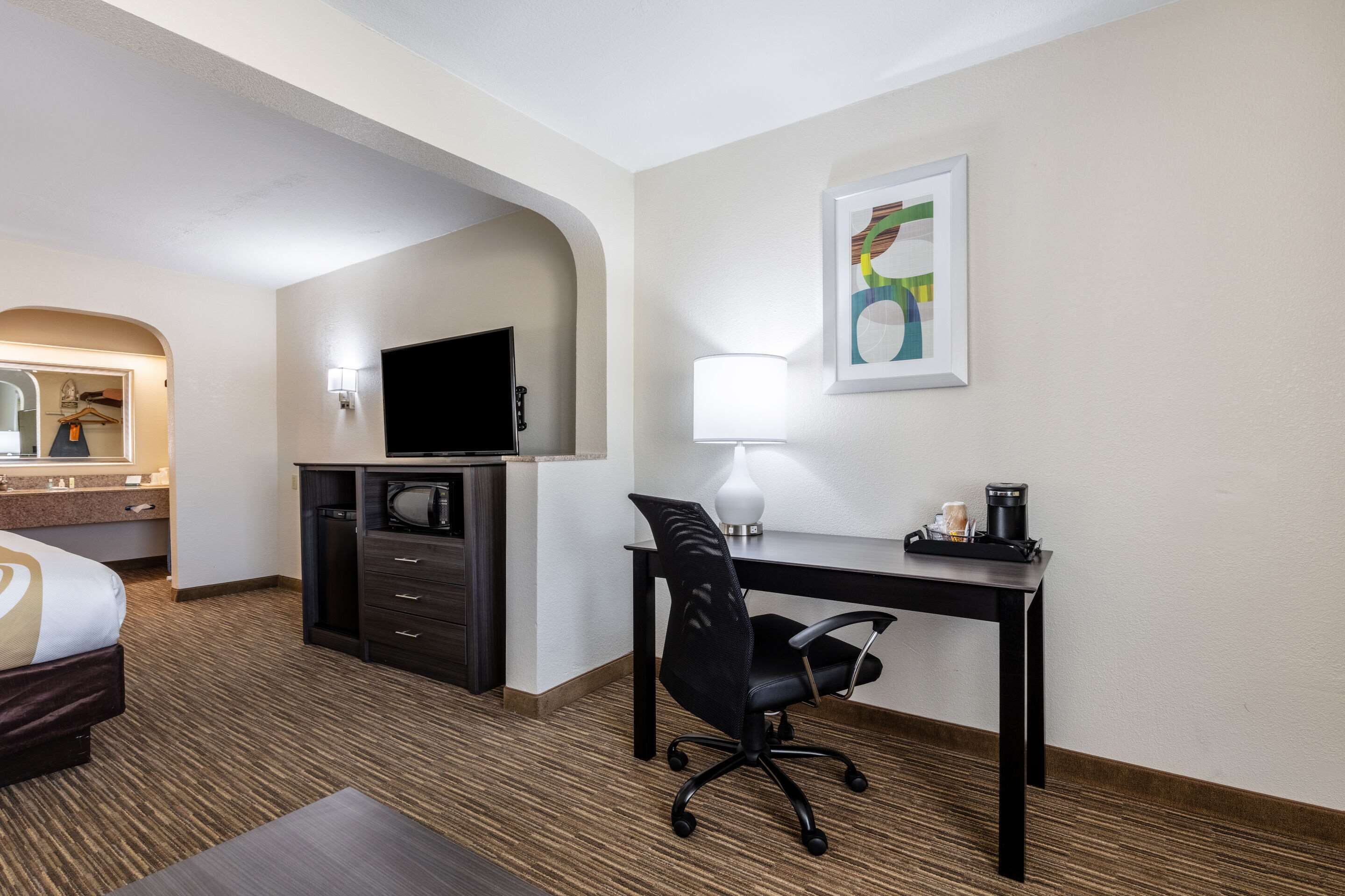 A hotel room with a bed, a desk with a chair, a TV, a lamp, and a coffee maker.