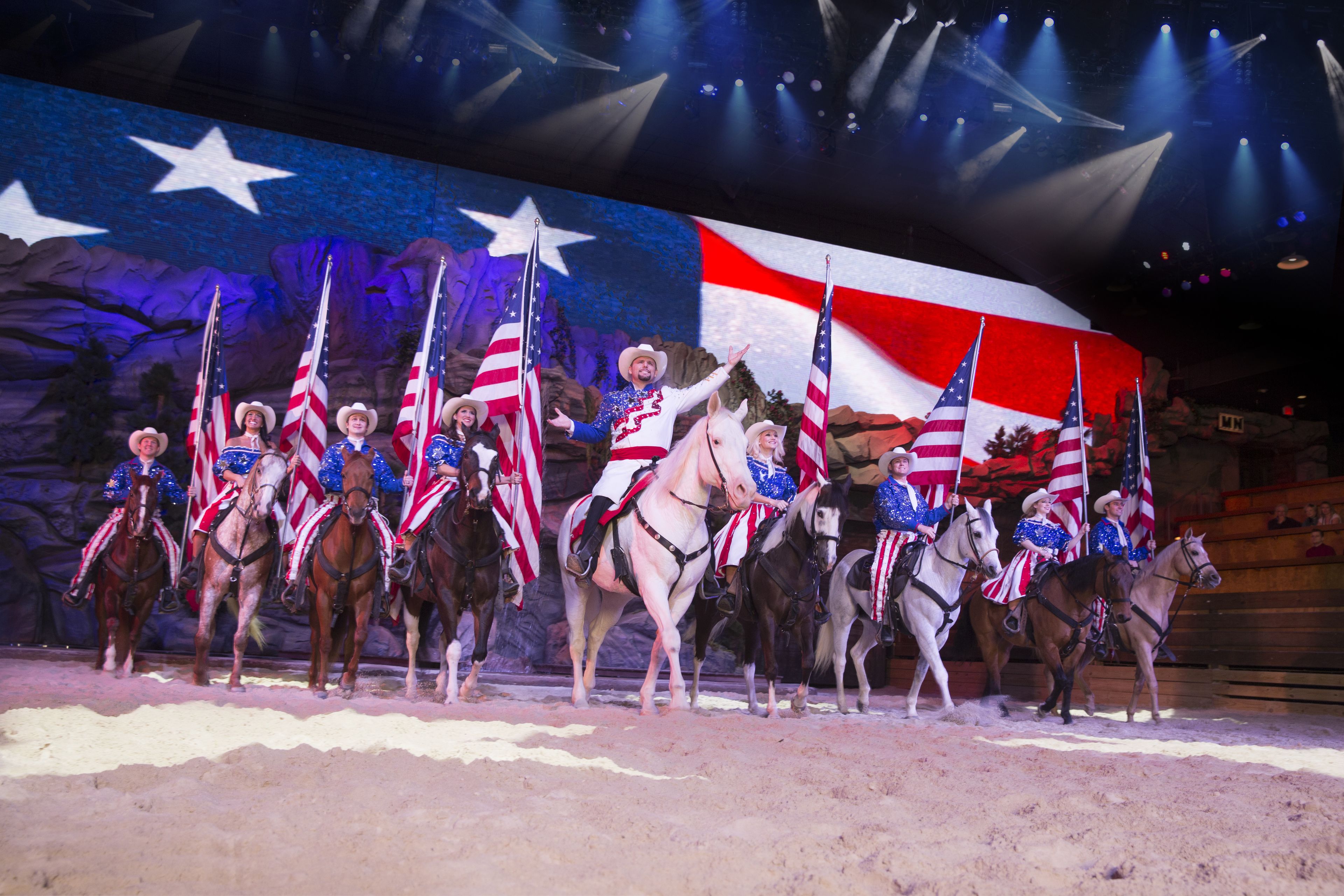 A stage with performers on horses, each holding an American flag.