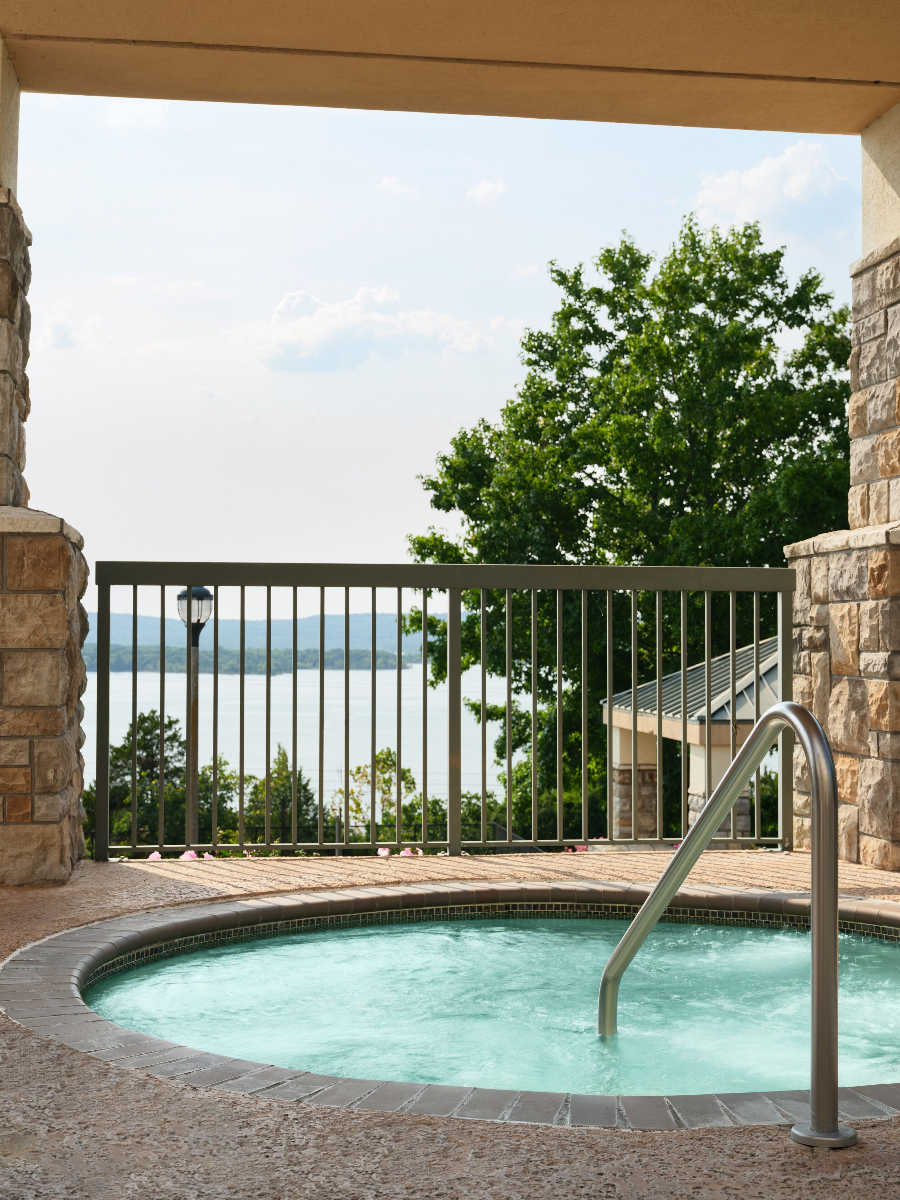 A pool with a metal railing, surrounded by stone walls and a view of a body of water.