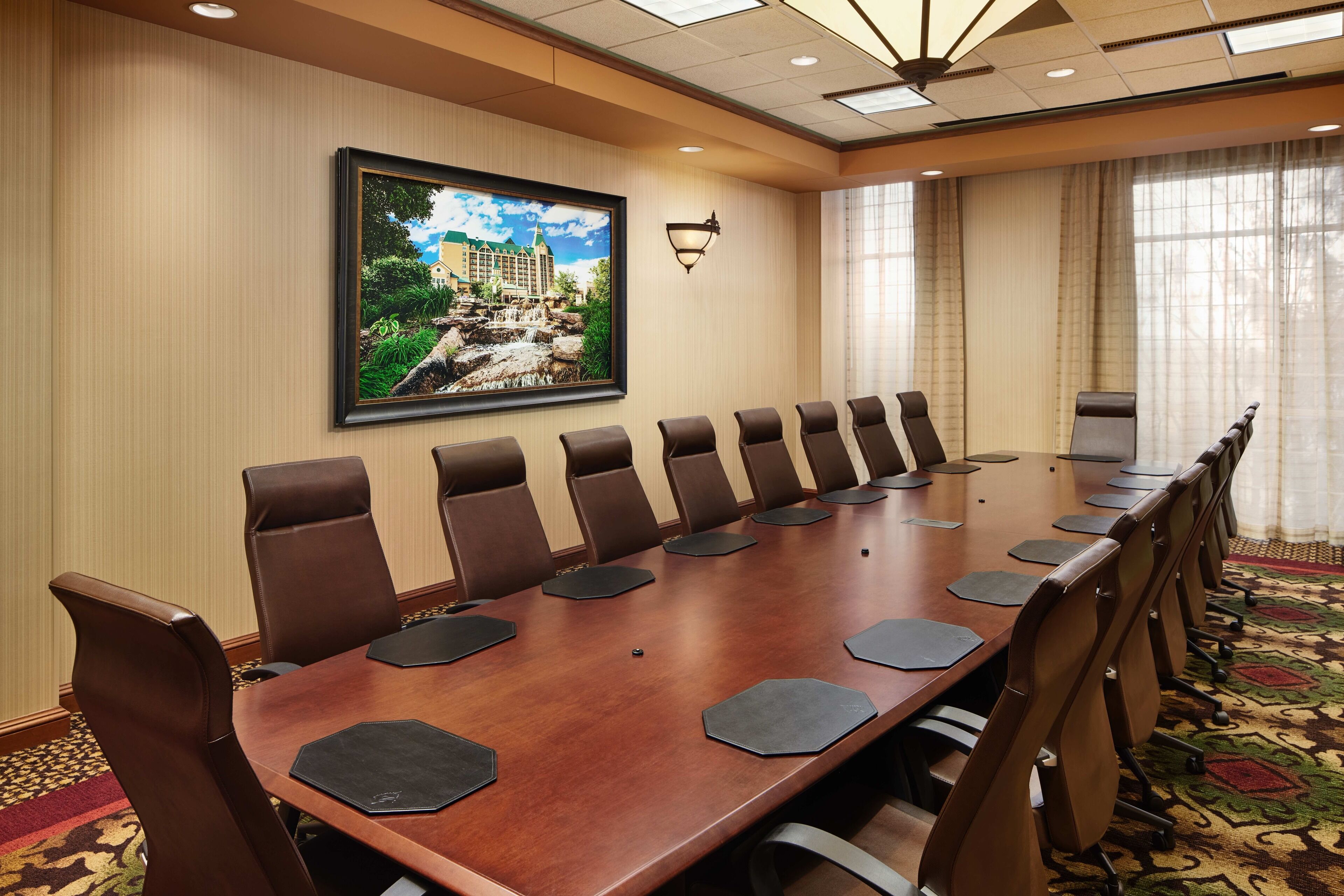 Een vergaderruimte met een lange tafel, meerdere stoelen en een groot gepresenteerd schilderij aan de muur.