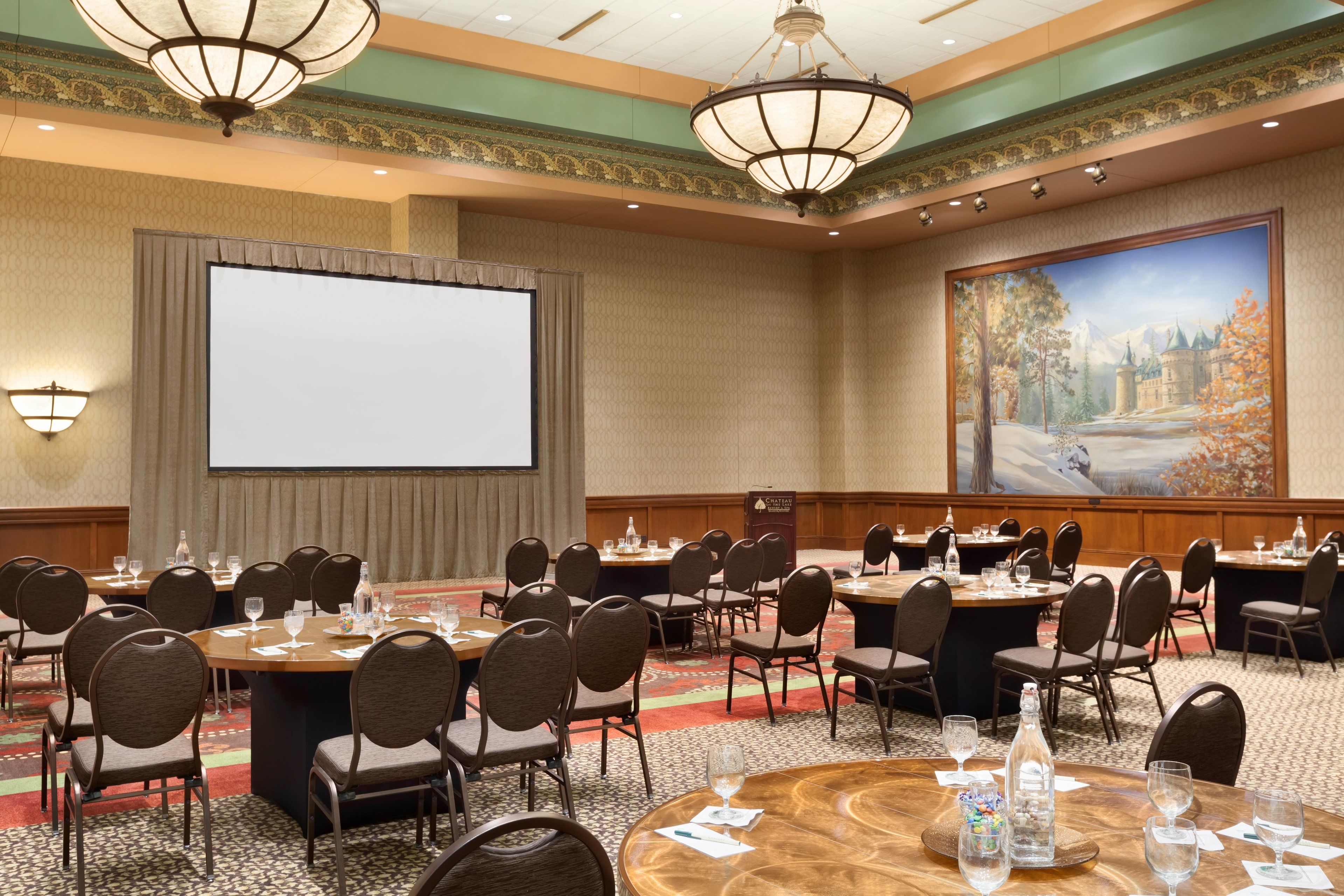 A conference room with multiple tables and chairs, a large screen, and a painting on the wall.