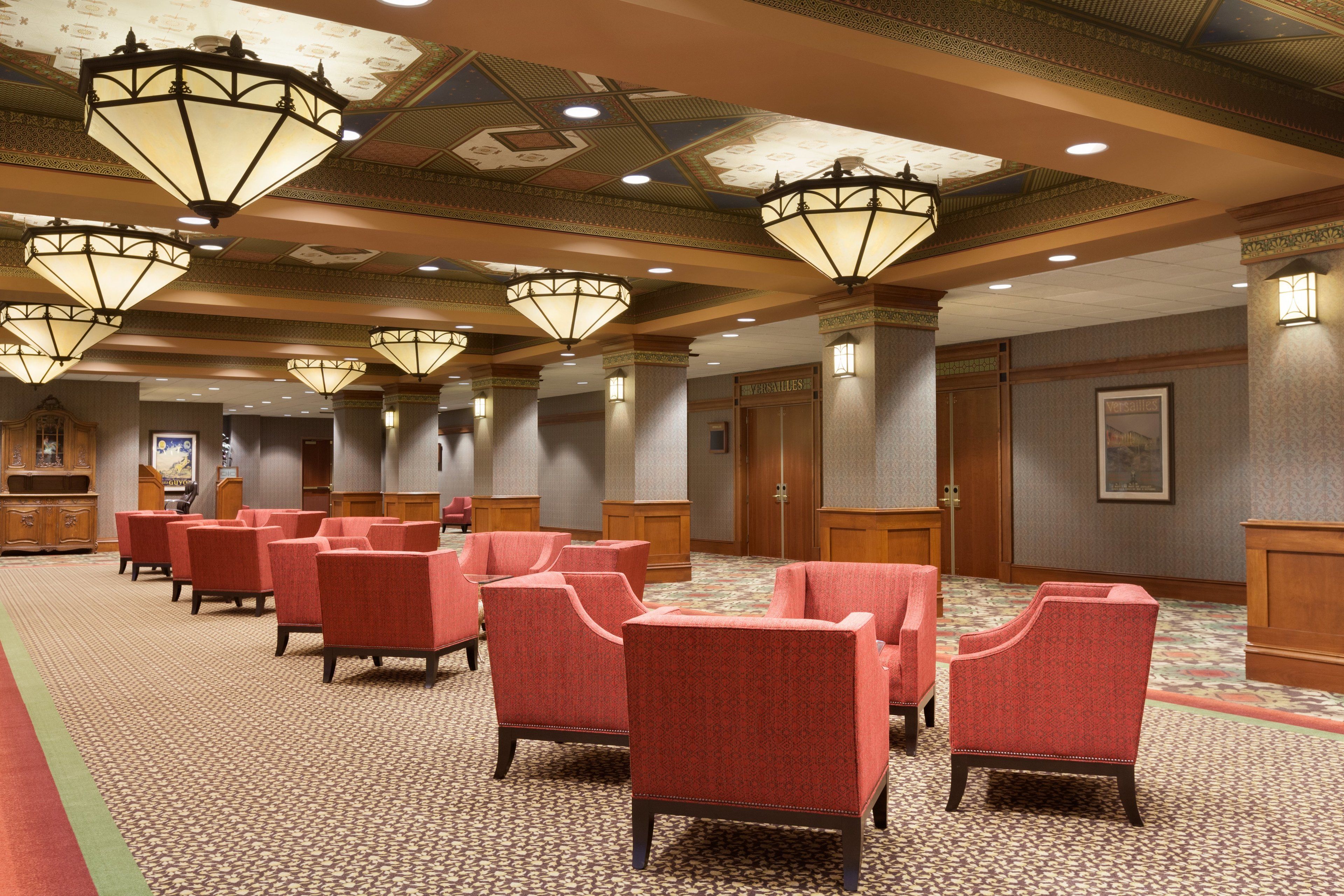 Un hall d’hôtel avec des fauteuils à revêtement rouge, une moquette à motifs et des luminaires décoratifs au plafond.