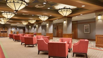 Un hall de hotel con sillones tapizados en rojo, alfombra estampada y lámparas de techo ornamentadas.