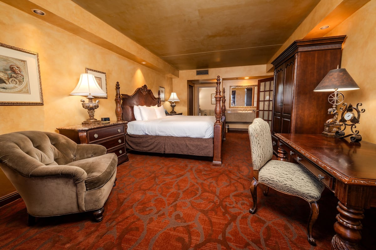A hotel room with a large bed, a wooden chair, a desk, and a dresser.