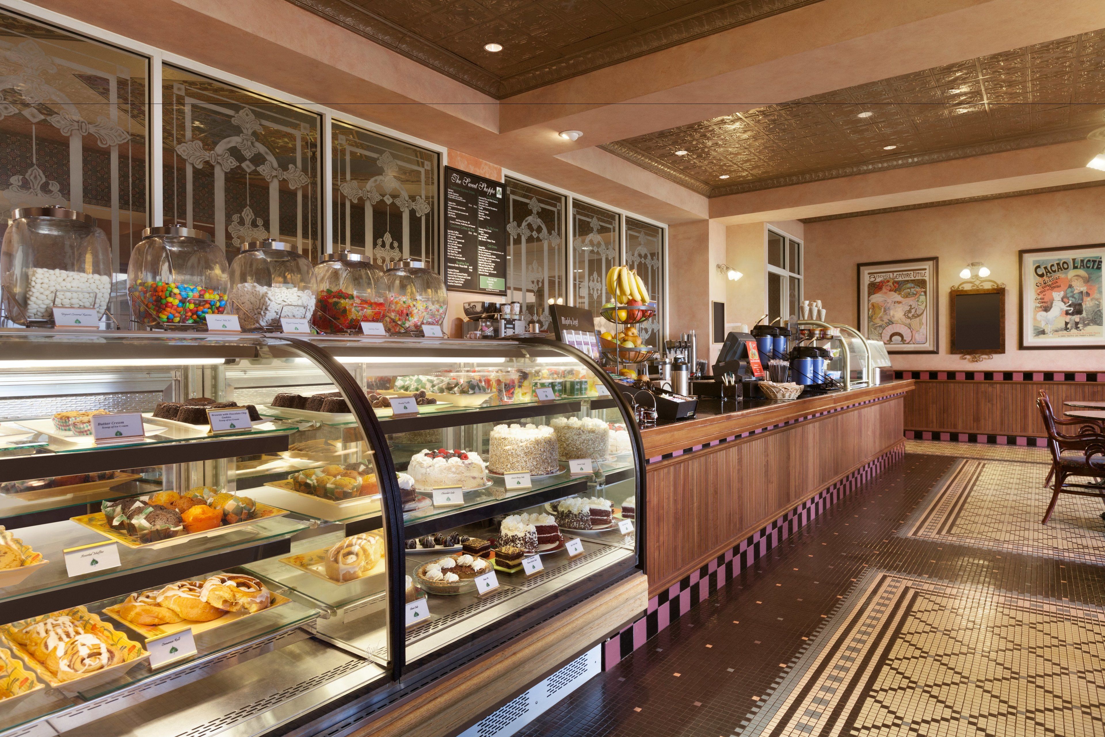 A bakery display case with various pastries and desserts, a wooden counter with a cash register, and a patterned floor.