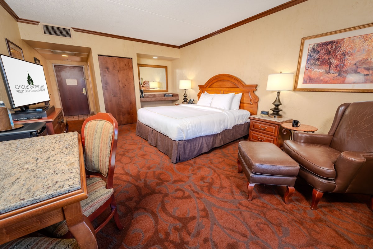 A hotel room with a bed, a desk, a chair, a sofa, and a carpeted floor.