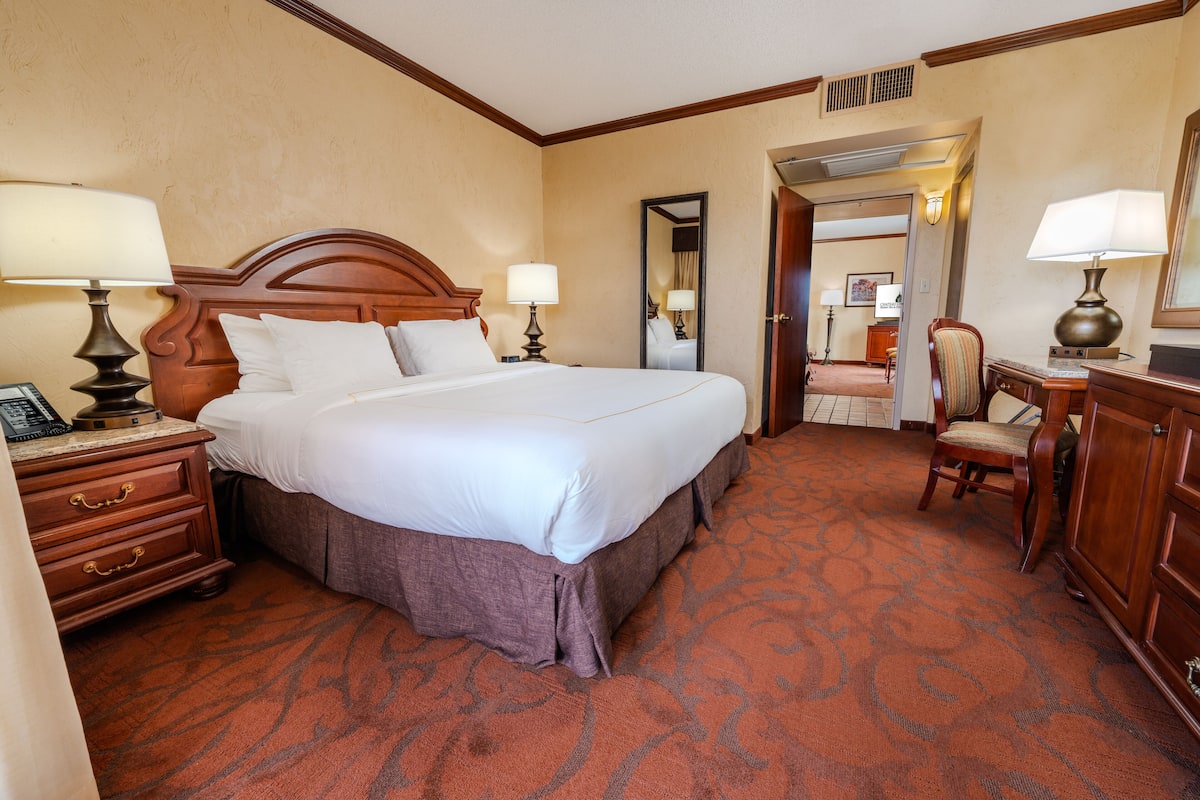 A hotel room with a large bed, two bedside tables with lamps, a wooden dresser, and a chair.