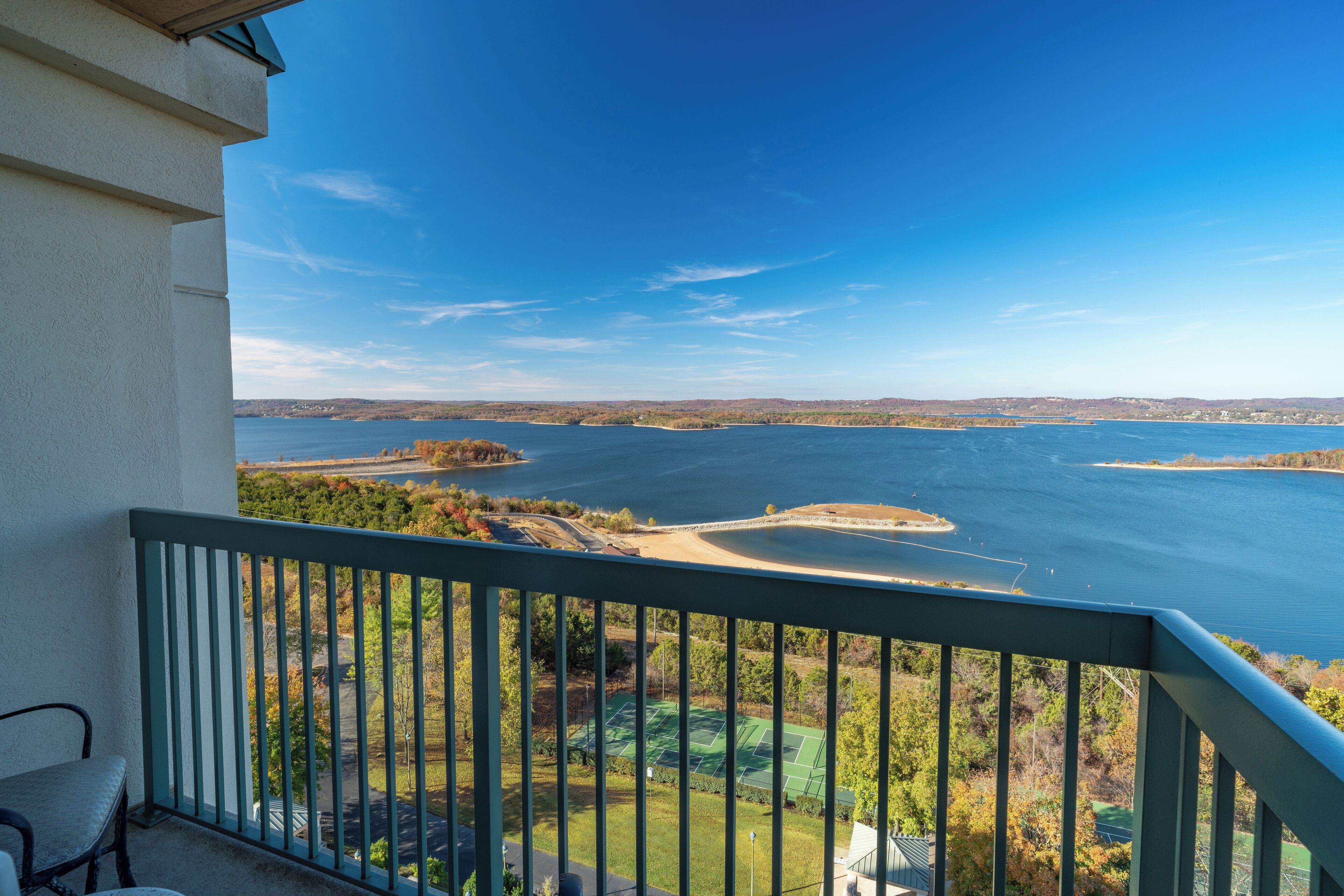 Ein Balkon mit Blick auf einen See, einen Tennisplatz und die umliegende Landschaft.