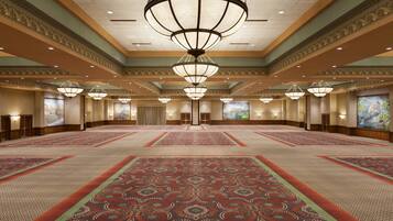 A spacious hotel lobby with a large, ornate chandelier, patterned carpet, and multiple doors leading to rooms.