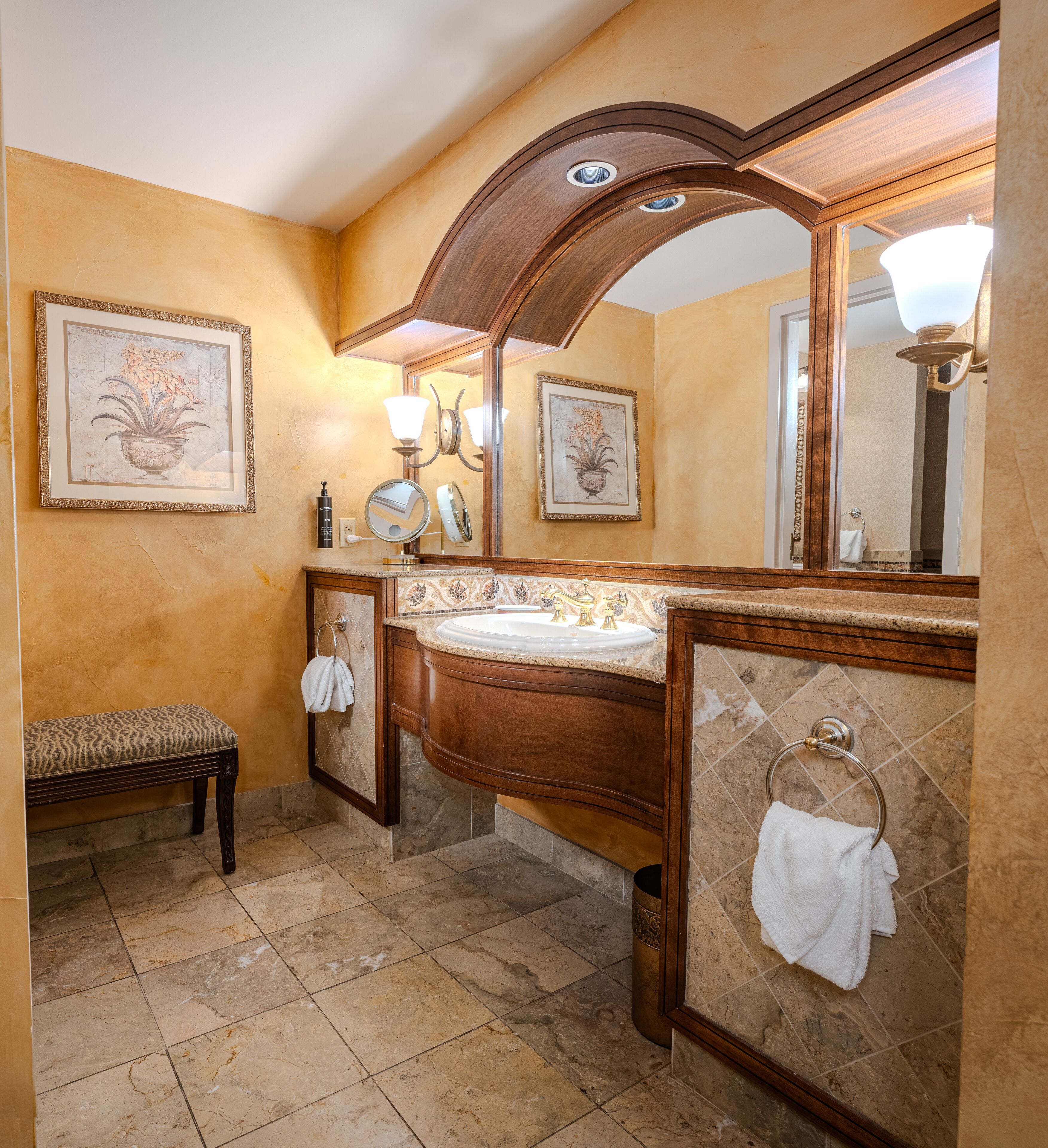 A bathroom with a wooden vanity, a large mirror, and a bench.