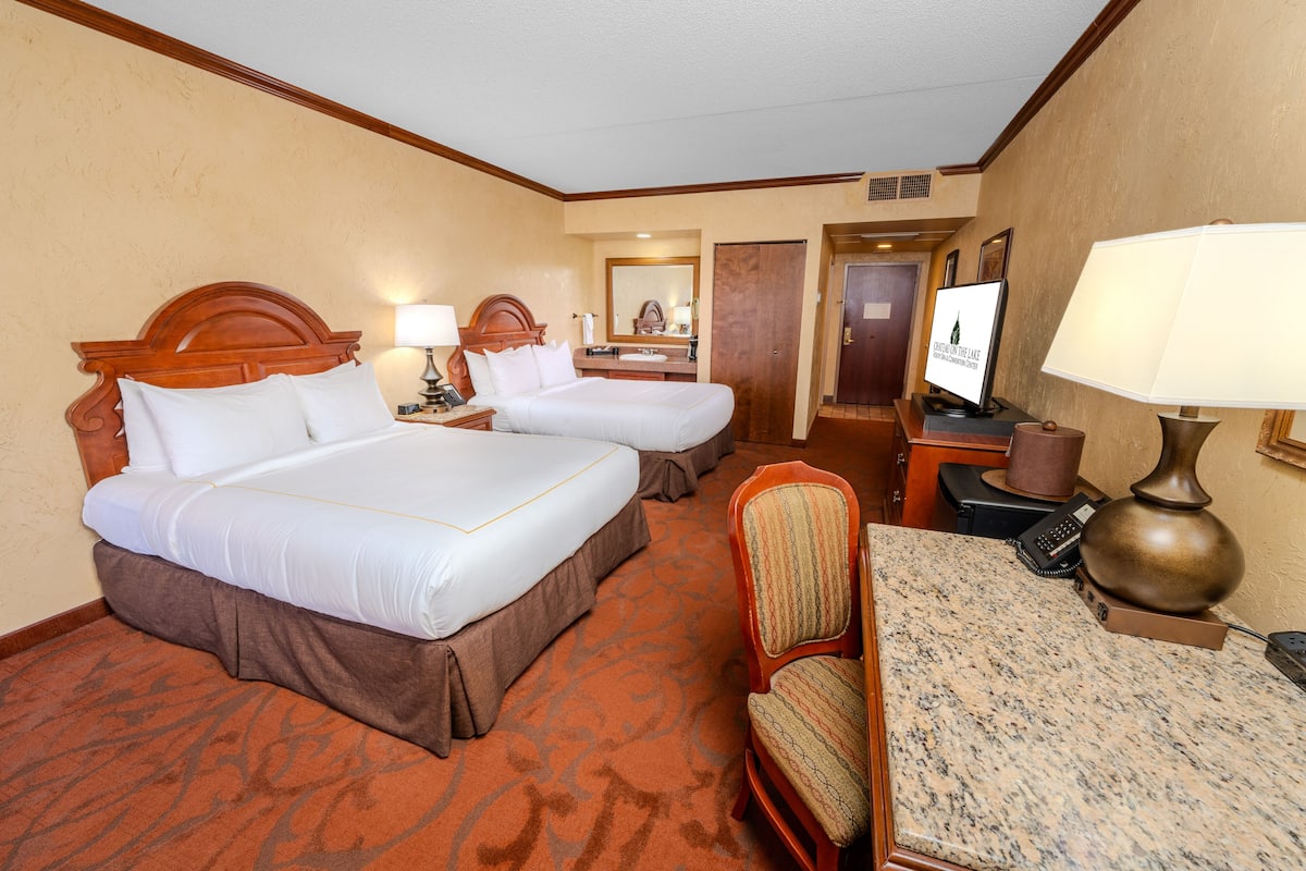 A hotel room with two beds, a desk with a lamp, a chair, a television, and a bathroom door.