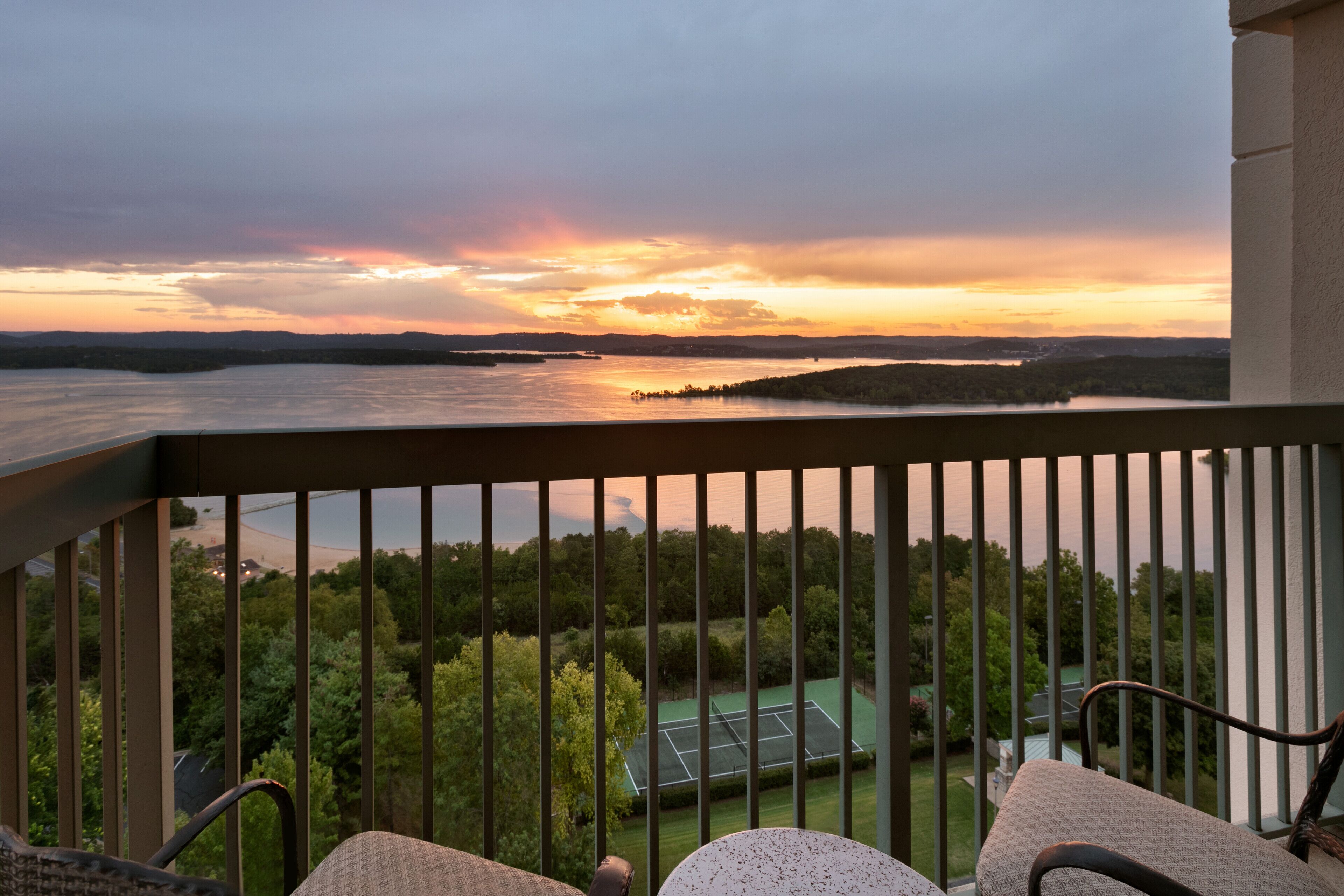 A balcony with a view of a lake and tennis court.