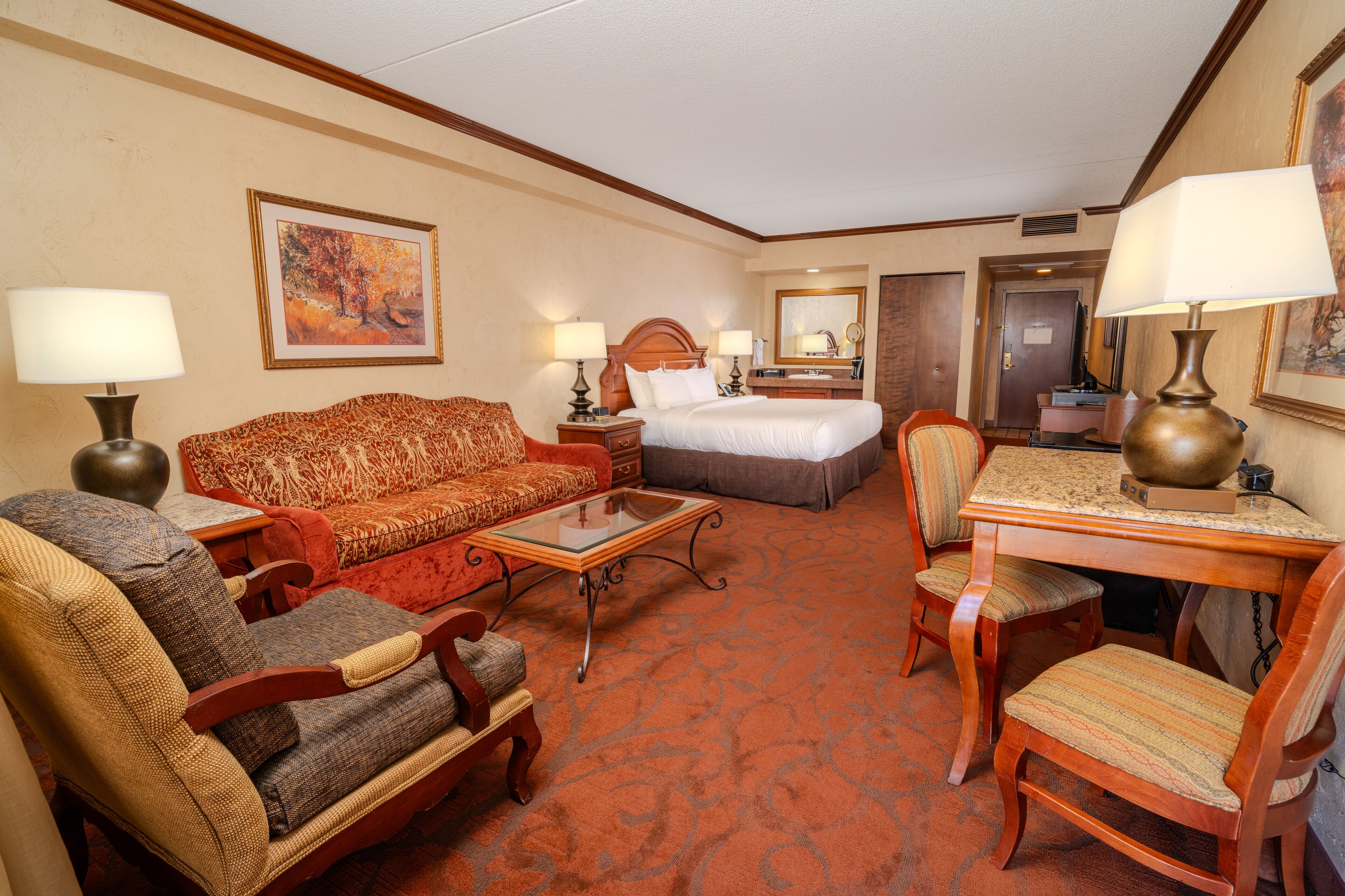 A hotel room with a bed, a sofa, a desk, and two chairs.