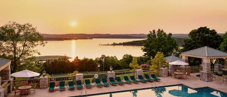 A pool area with lounge chairs and a view of a lake at sunset.