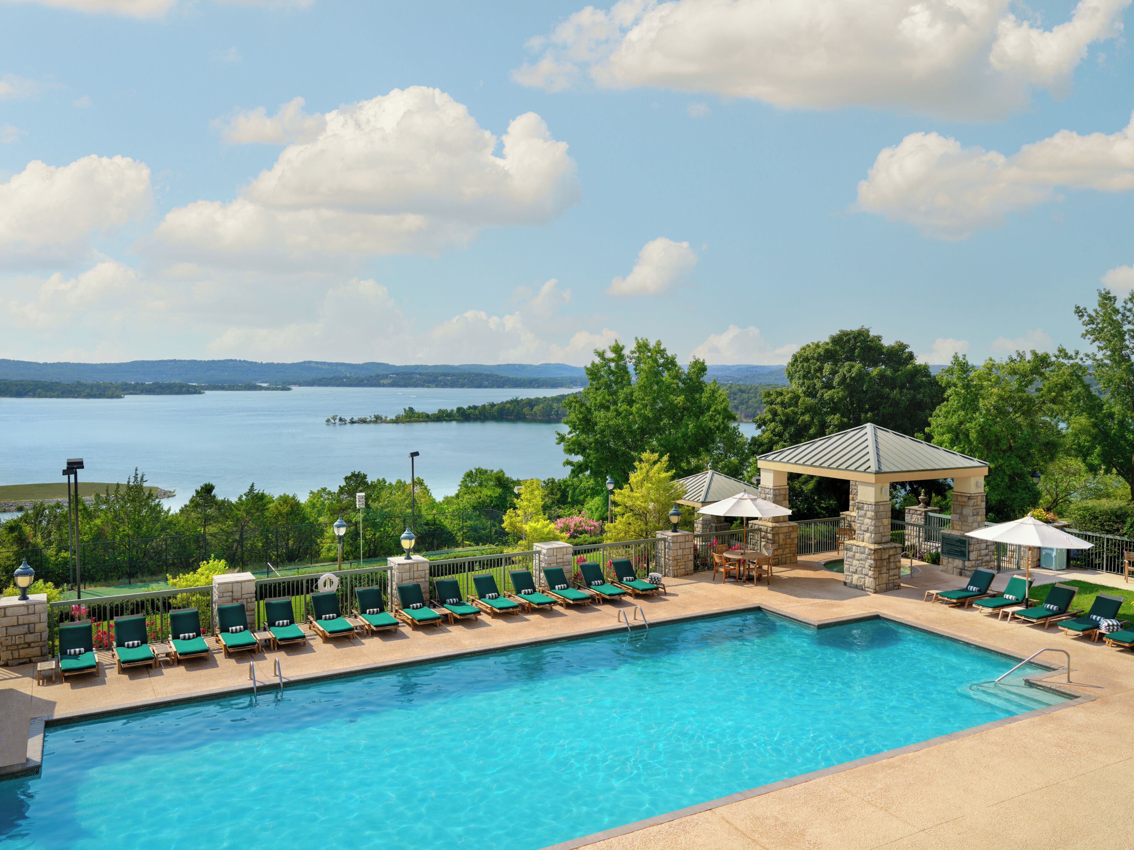 Piscina con sillas de descanso y un pabellón, con vistas a un lago.