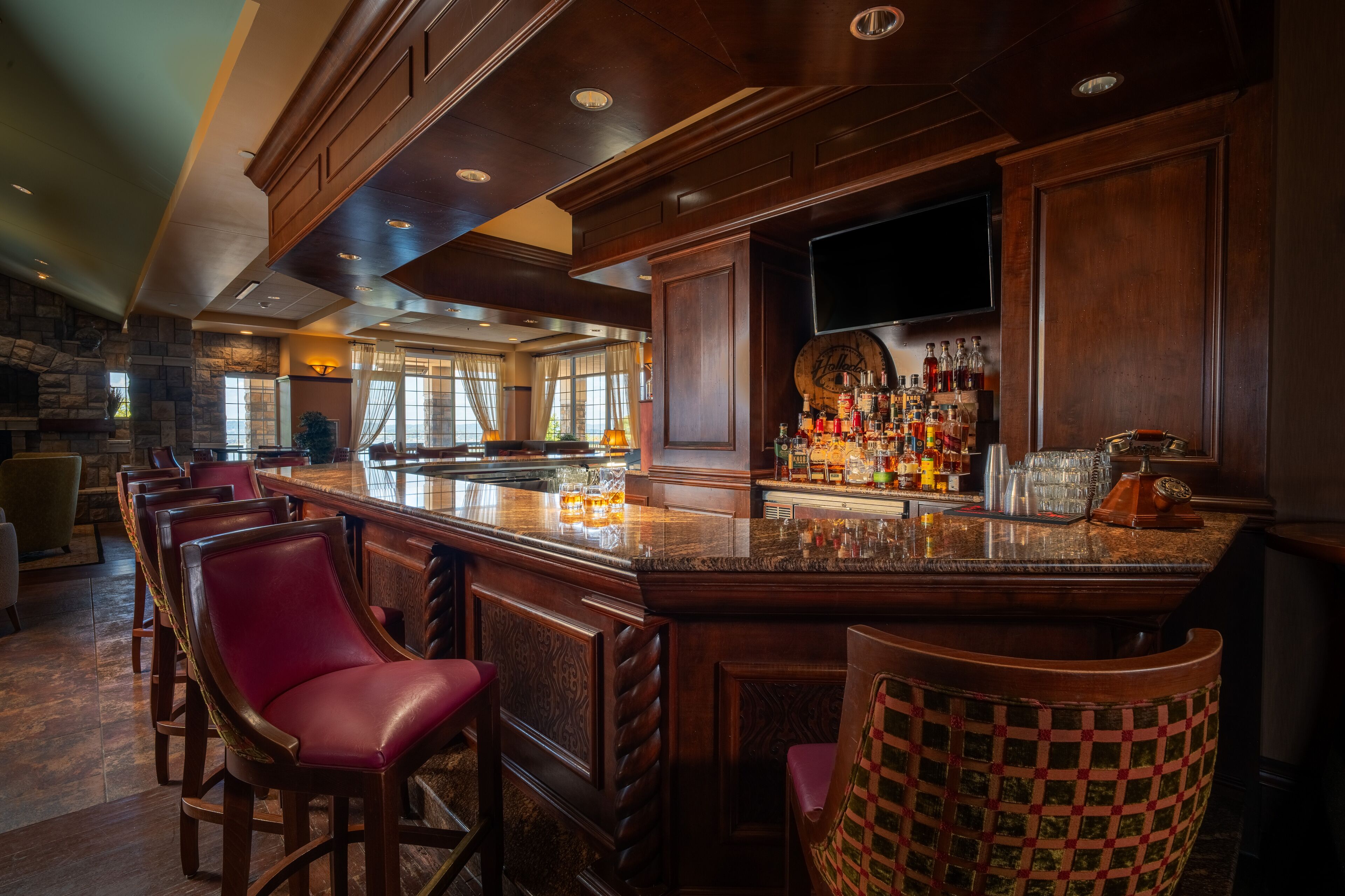 A bar area with a stone fireplace, wooden bar counter, and leather bar stools.