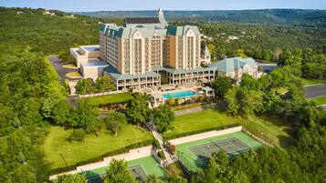 A large hotel with multiple buildings, a swimming pool, tennis courts, and surrounding greenery.