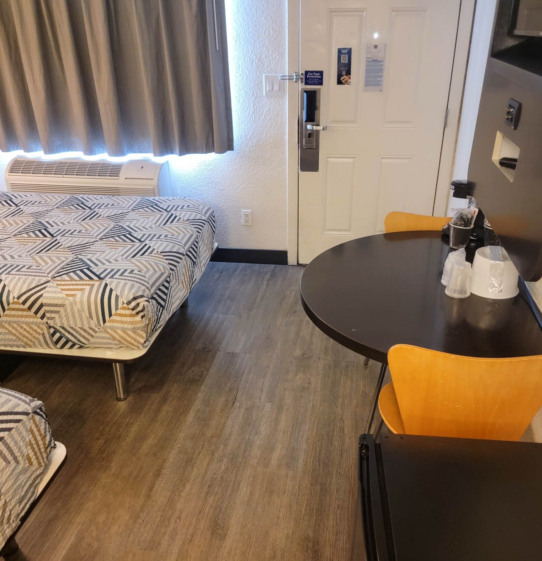 Une pièce comprenant un lit, une table avec des chaises, une porte et une fenêtre avec des rideaux.